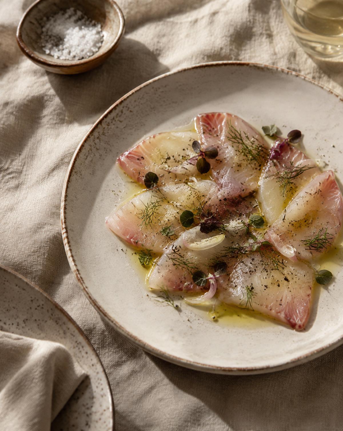 Kingfish crudo with fennel and olive oil on a ceramic plate